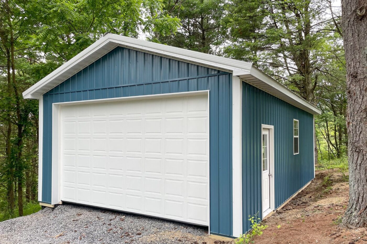 Blue pole barn shed with white garage door, trim, and single door on side