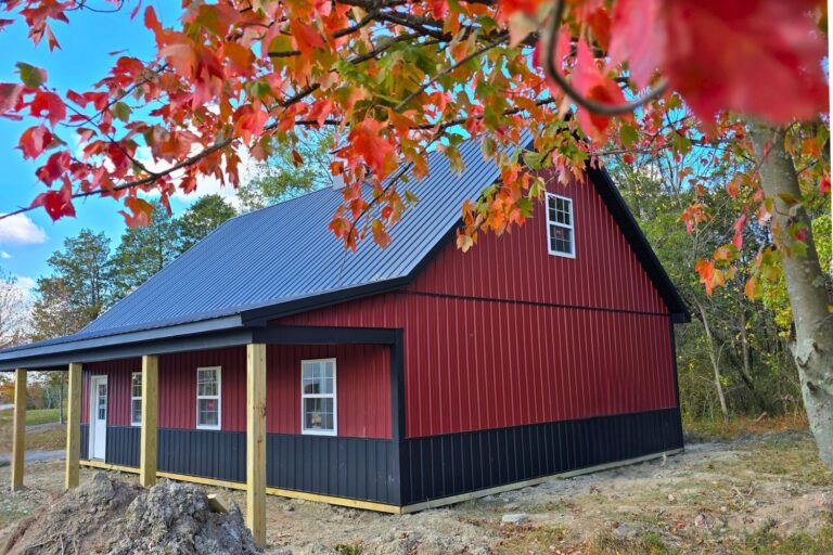 An extremely good pole barn builder and their red and brown barn with overhang under autumn leaves