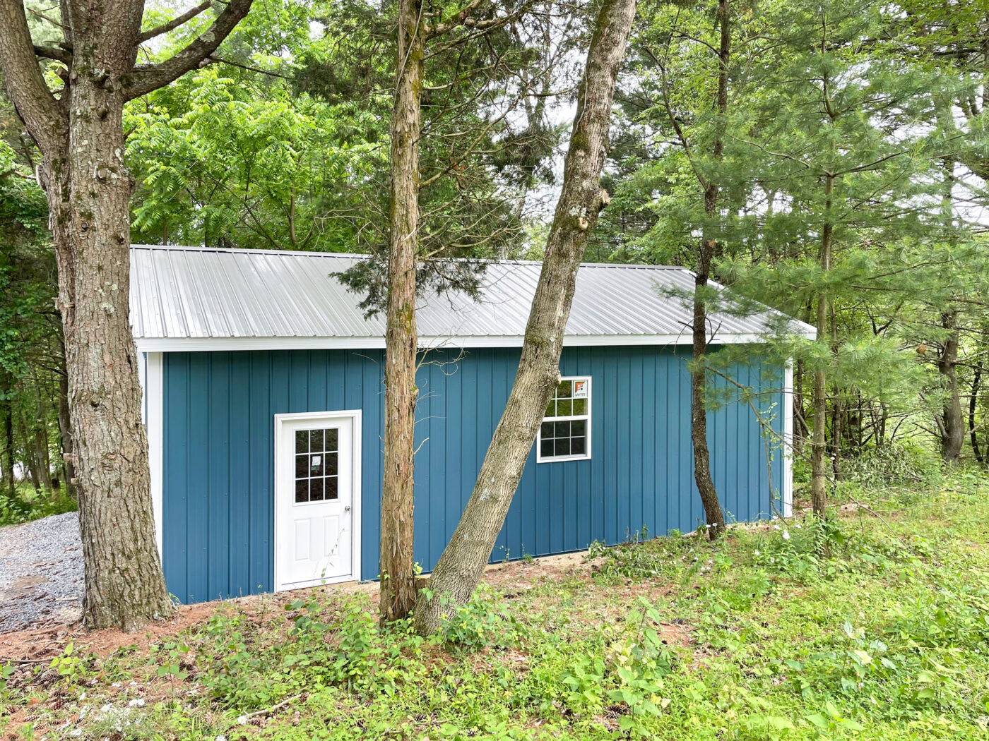 blue and white pole barn garage in Saylorsburg PA behind the trees in the woods on a hill